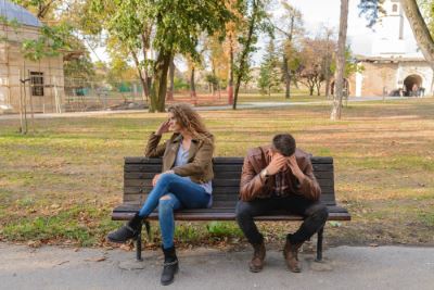 Man sad on a bench, woman looking the away in disapointment